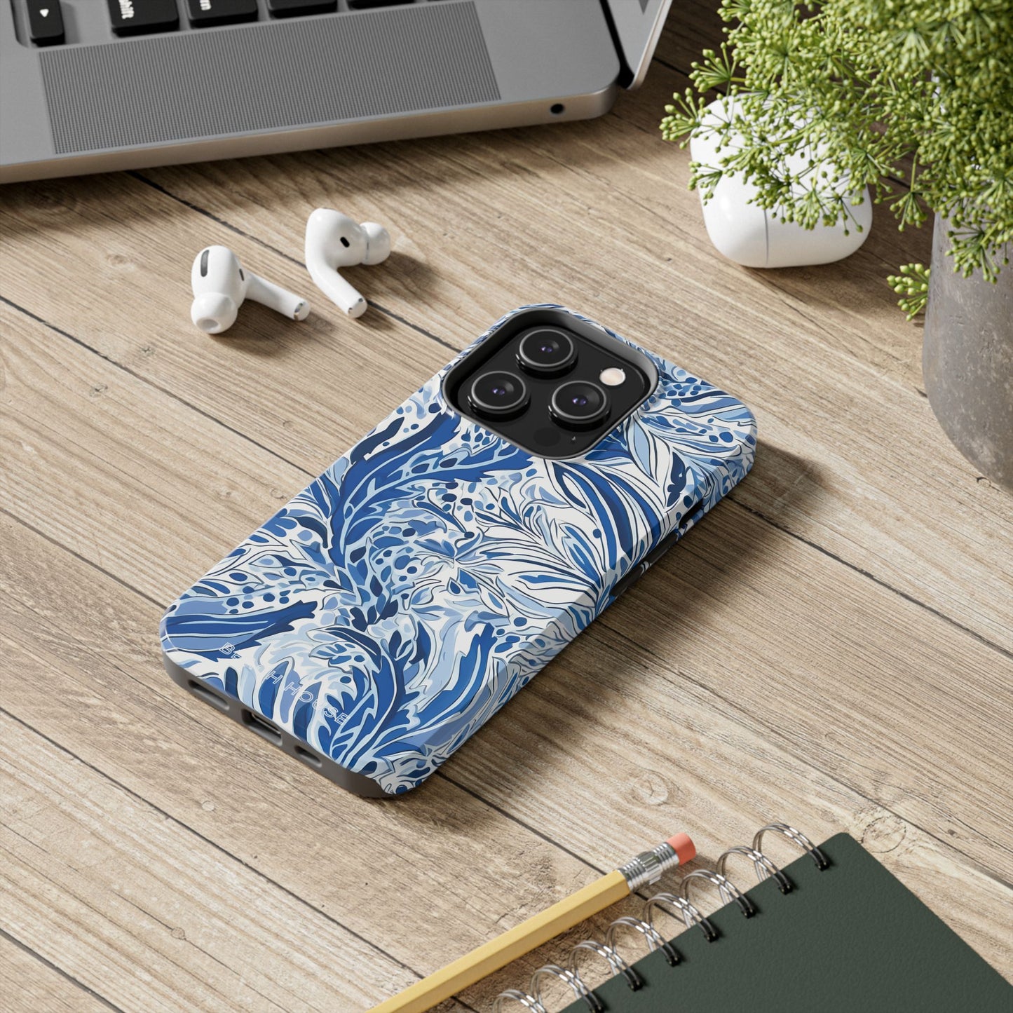 Nags Head case for iPhone on a wooden desk with AirPods, laptop, and notebook.