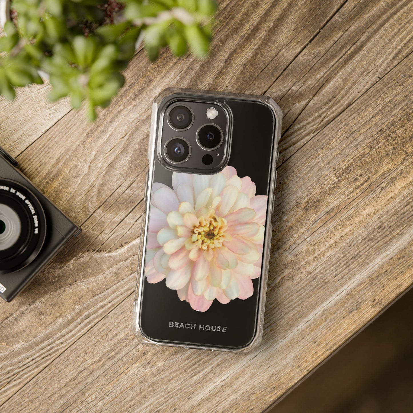 Phone case with floral design on a wooden surface next to a camera