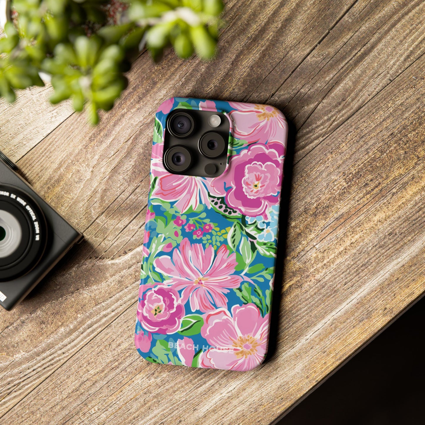 Floral Madeira Slim Case for iPhone on a wooden surface with a camera and plant in the background