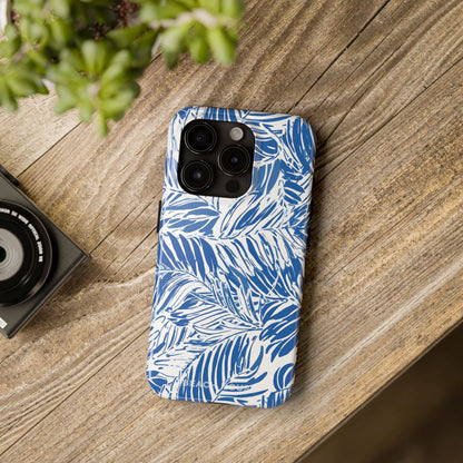 Blue and white palm leaf patterned Hampton Tough Case for iPhone on a wooden surface with a camera and plant in the background.