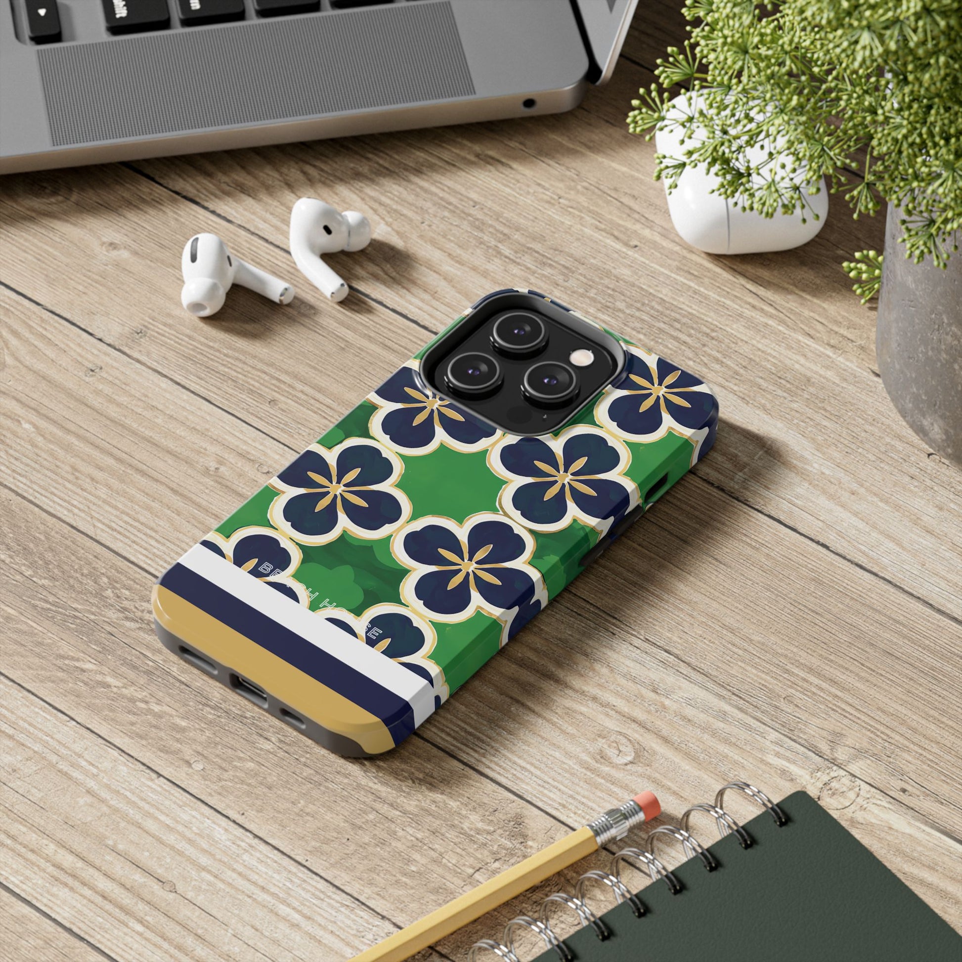 South Bend Tough Case for iPhone with floral design on a wooden surface with laptop, earbuds, and notebook.