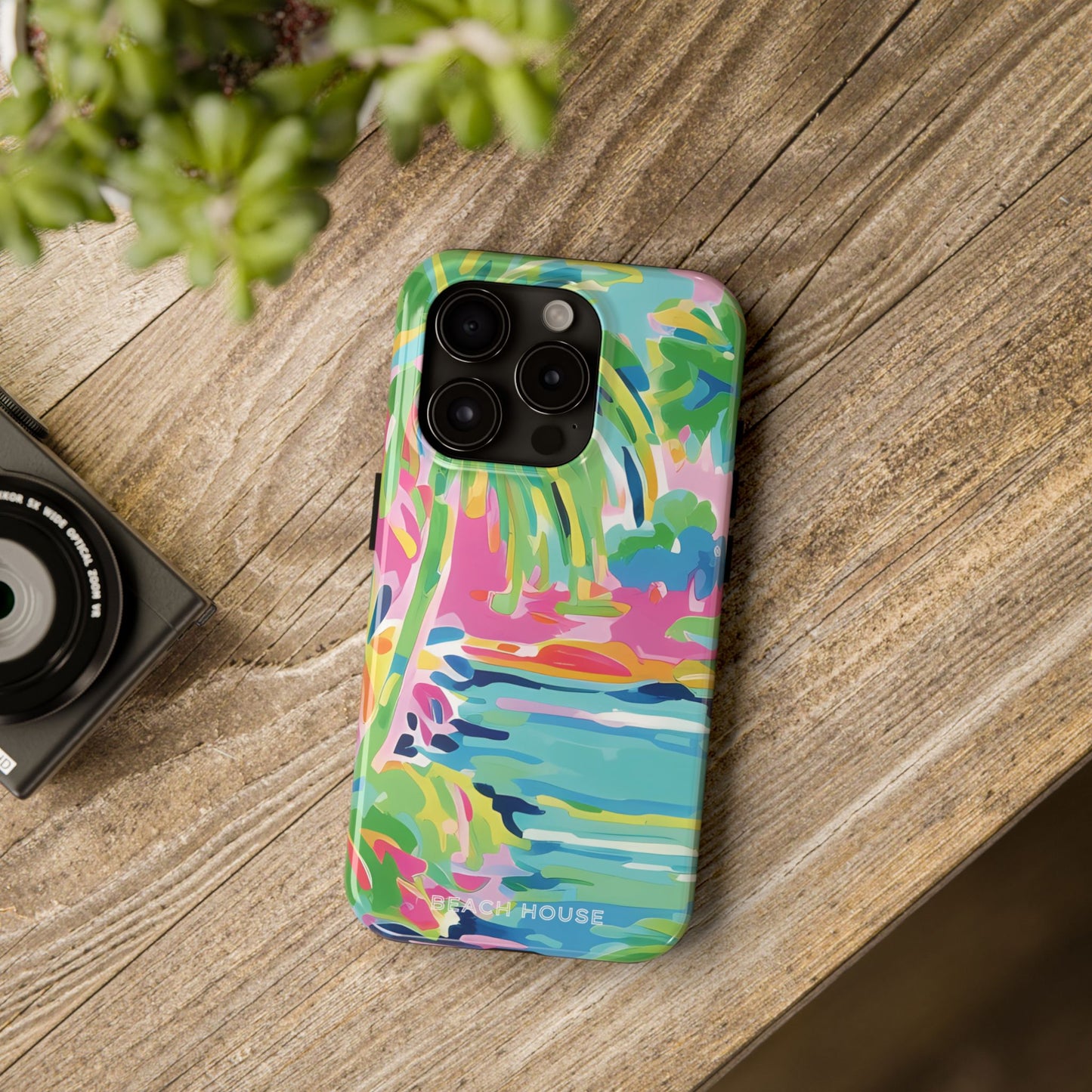 Colorful Delray phone case on a wooden surface with a camera and plant in the background
