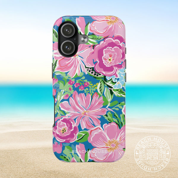Madeira Tough Case for iPhone 17 with pink and green flowers on a blue background, placed on sand with ocean view.