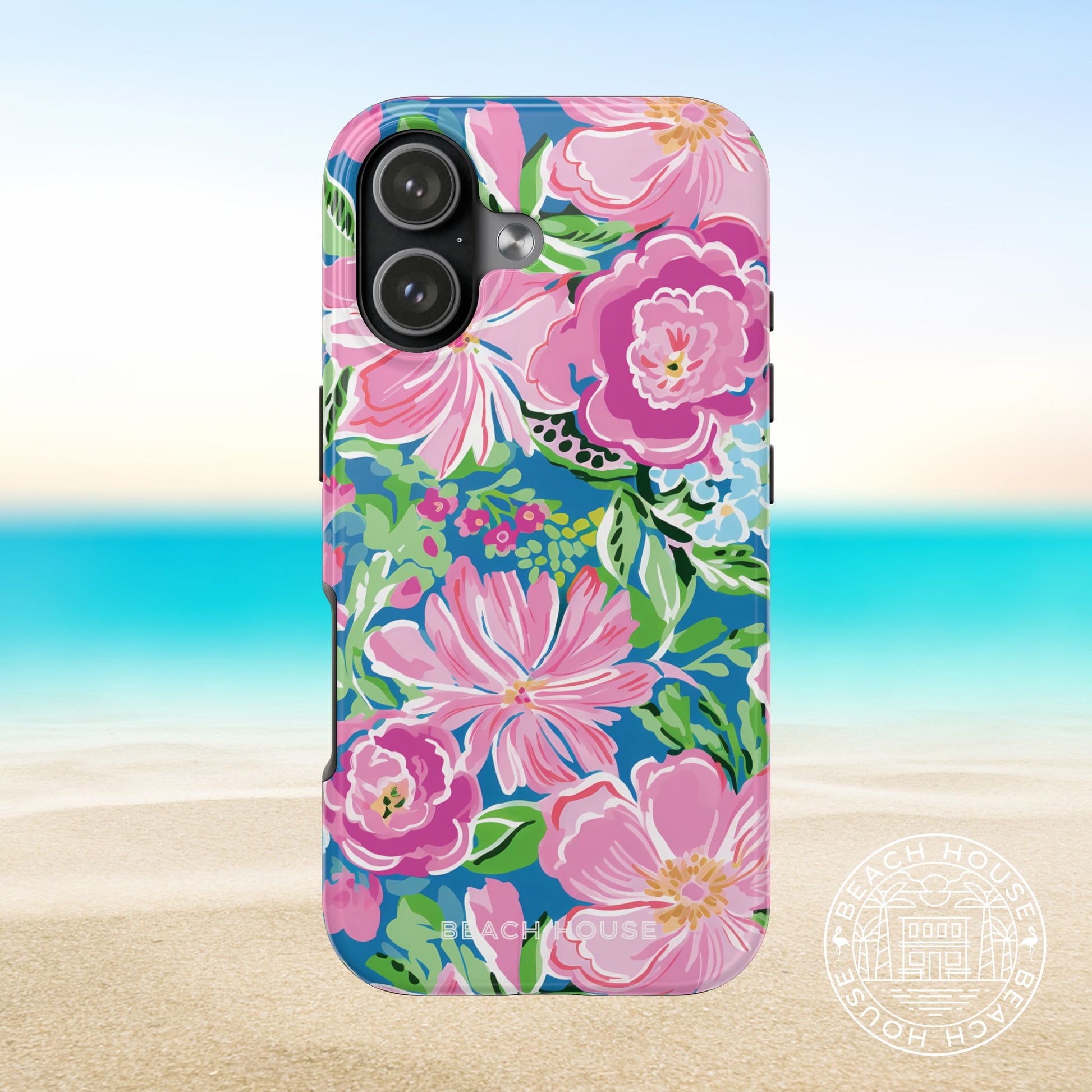 Madeira Tough Case for iPhone 17 with pink and green flowers on a blue background, placed on sand with ocean view.