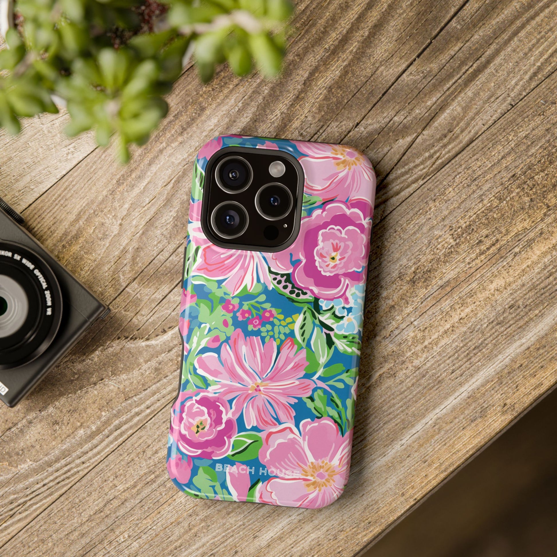 Floral Madeira MagSafe Tough Case for iPhone on a wooden surface with a camera and plant in the background