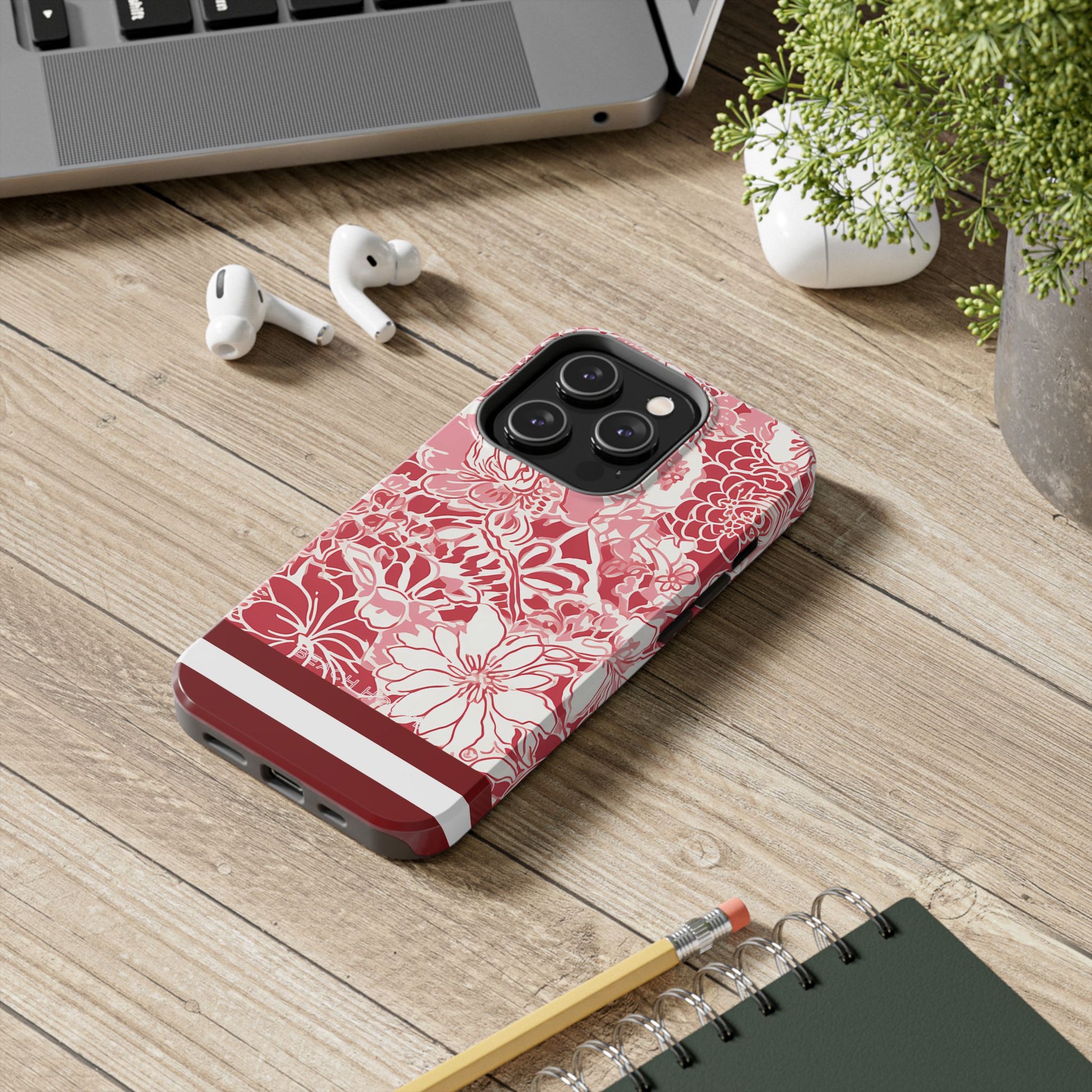Norman Tough Case for iPhone with floral design on a wooden surface with laptop, earbuds, and notebook.