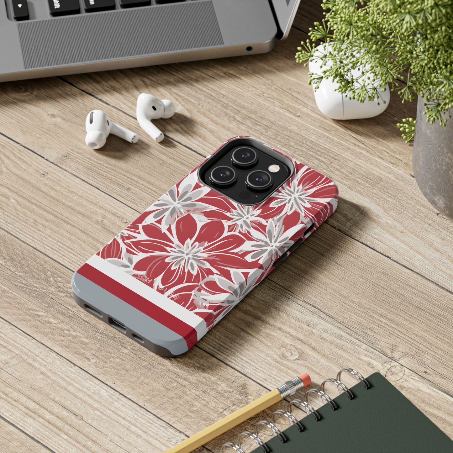 Columbus Tough case for iPhone with red and white floral pattern on a wooden surface with laptop, earbuds, and notebook.