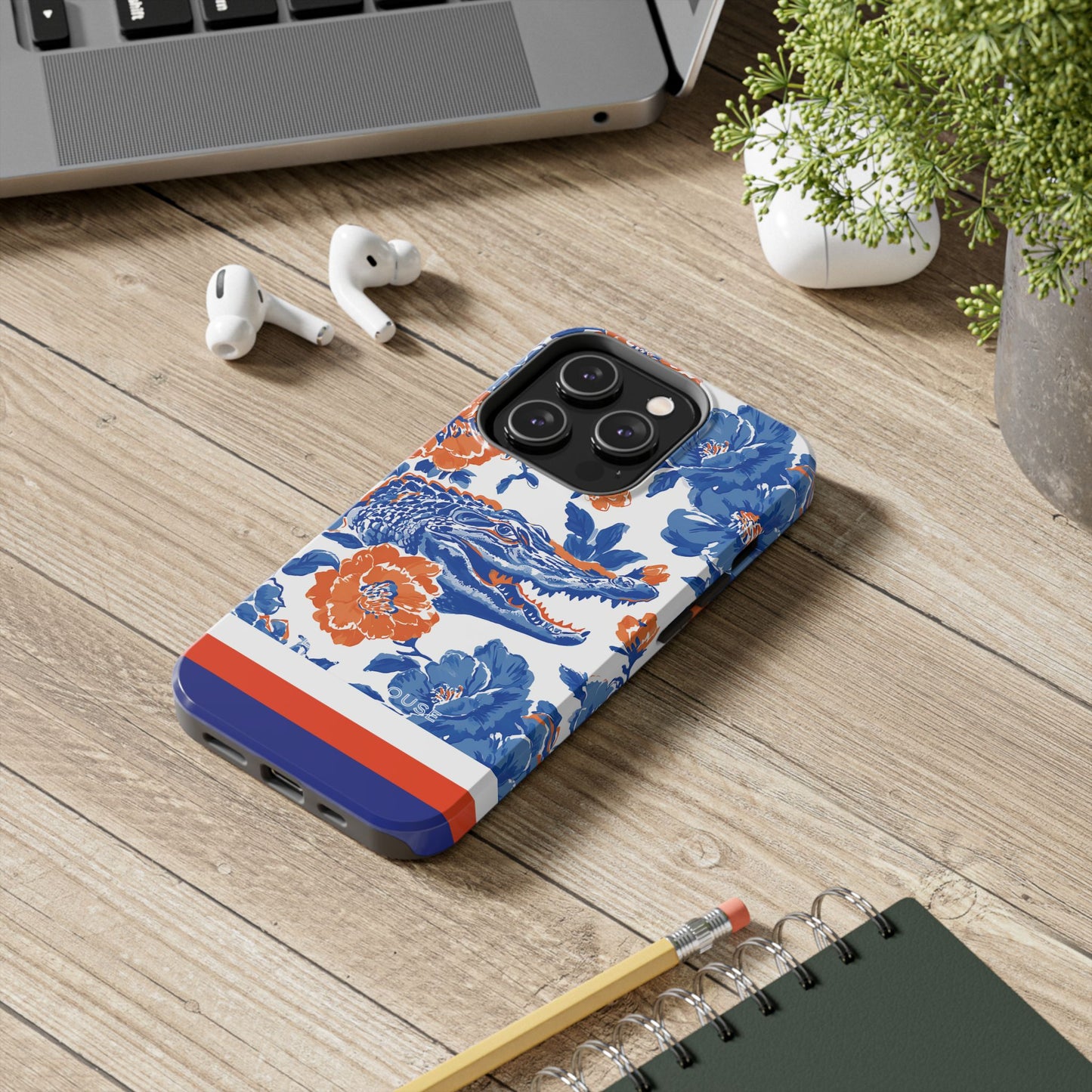 Phone case with floral design on a wooden surface with laptop, earbuds, and notebook.