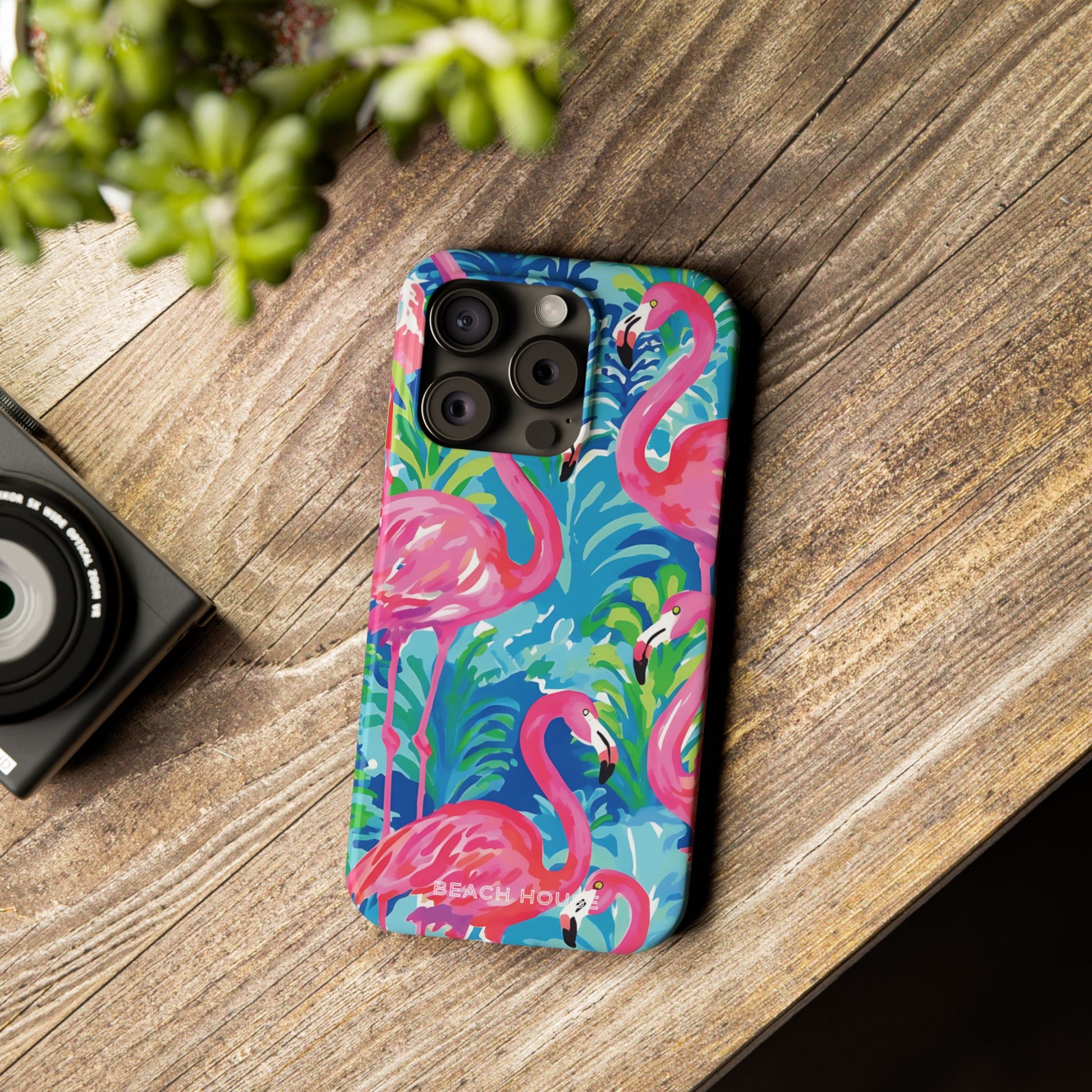Colorful Key Largo Slim Case for iPhone with flamingo design on a wooden surface next to a camera.
