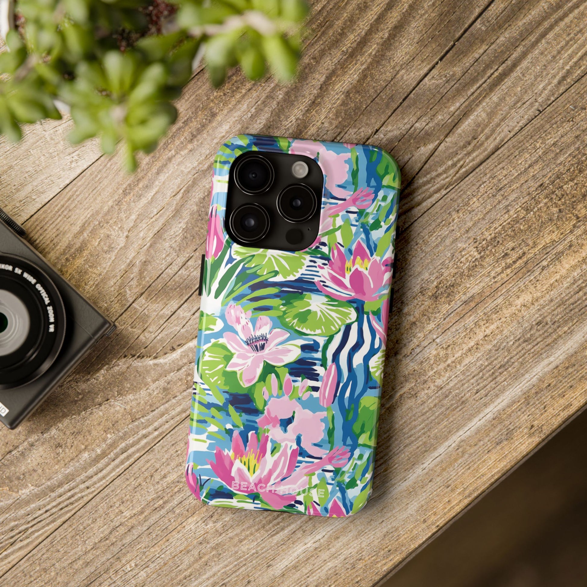 Colorful floral Everglades Tough Case for iPhone on a wooden surface with a camera and plant in the background