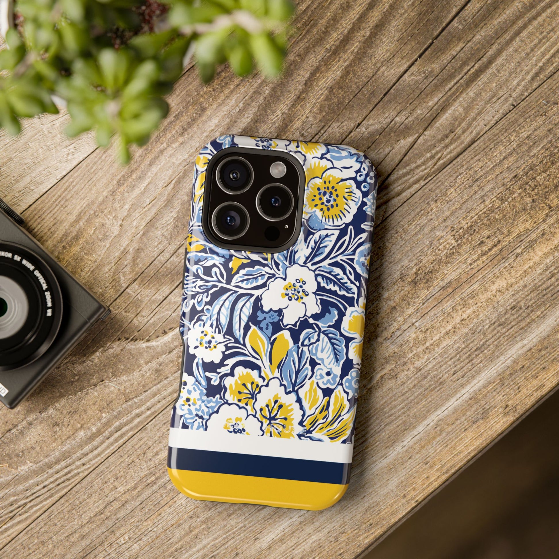 Ann Arbor MagSafe Tough Case for iPhone, blue and yellow floral design on a wooden surface with a camera and plant in the background
