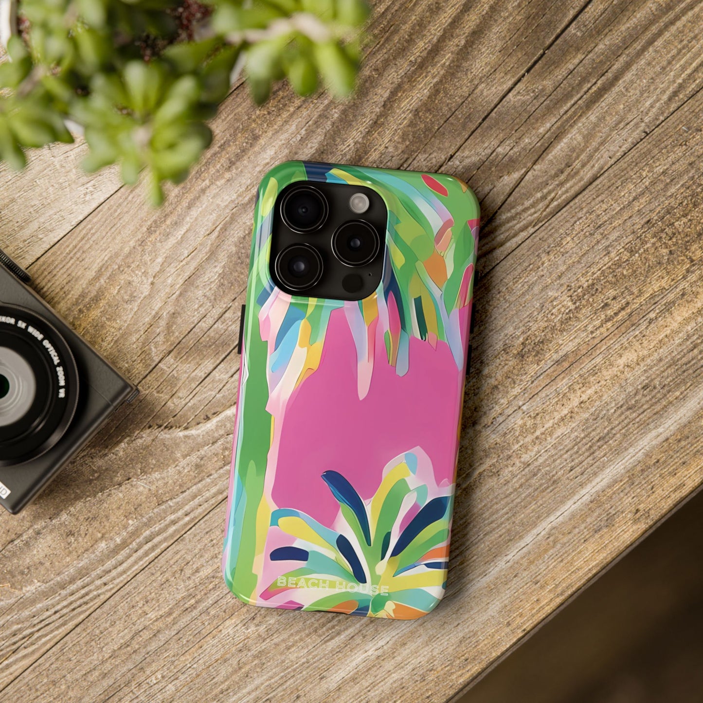 Colorful Boca phone case on a wooden surface with a camera and plant in the background