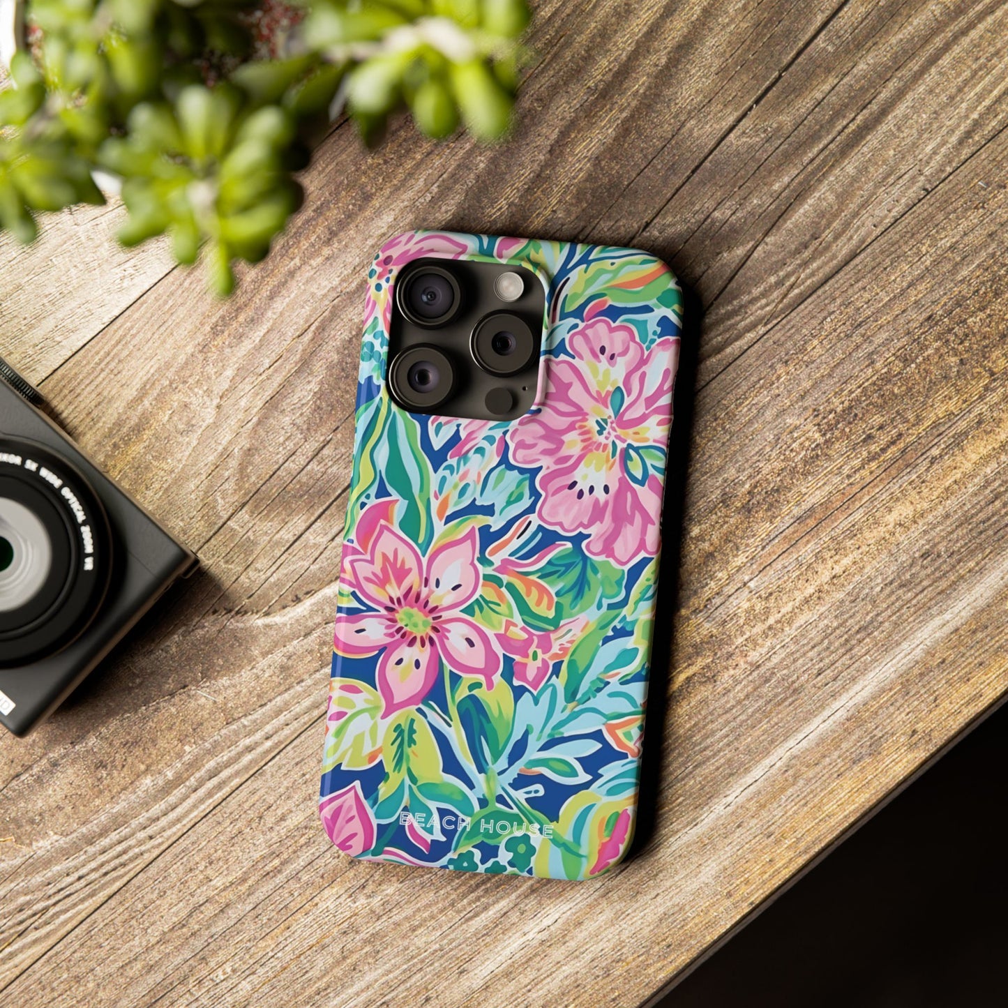 Floral Fernandina Slim Case for iPhone on a wooden surface with a camera and plant in the background