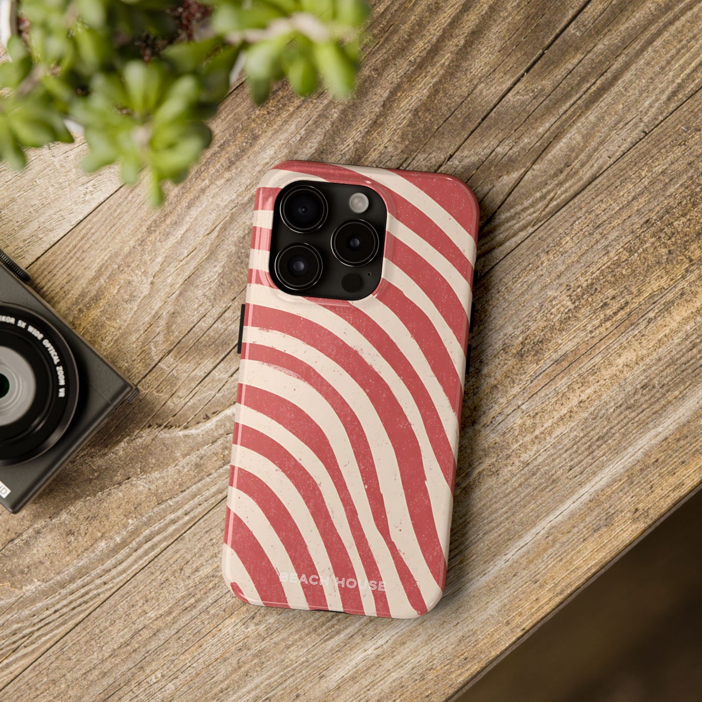 Kure Beach Phone case with red and white striped pattern on a wooden surface with a camera and plant.