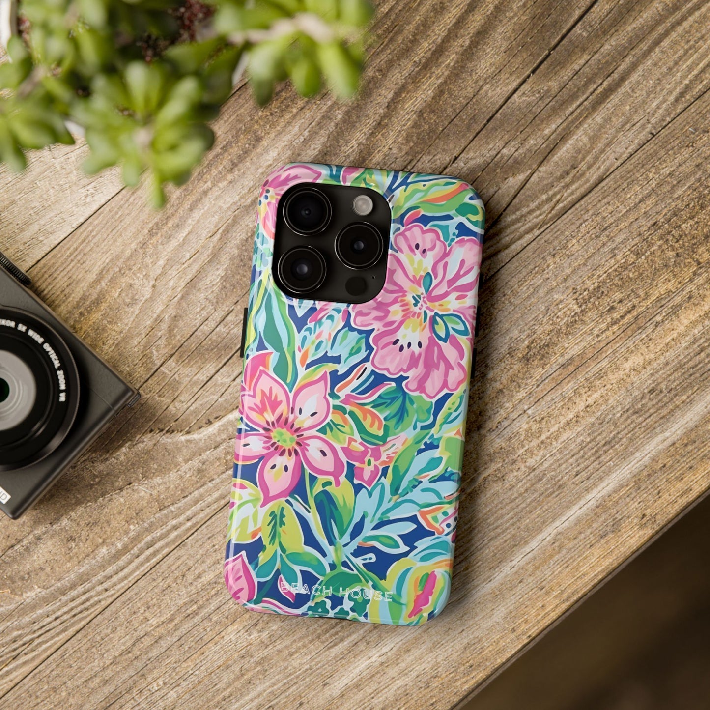 Colorful floral Fernandina Tough Case for iPhone case on a wooden surface with a camera and plant in the background