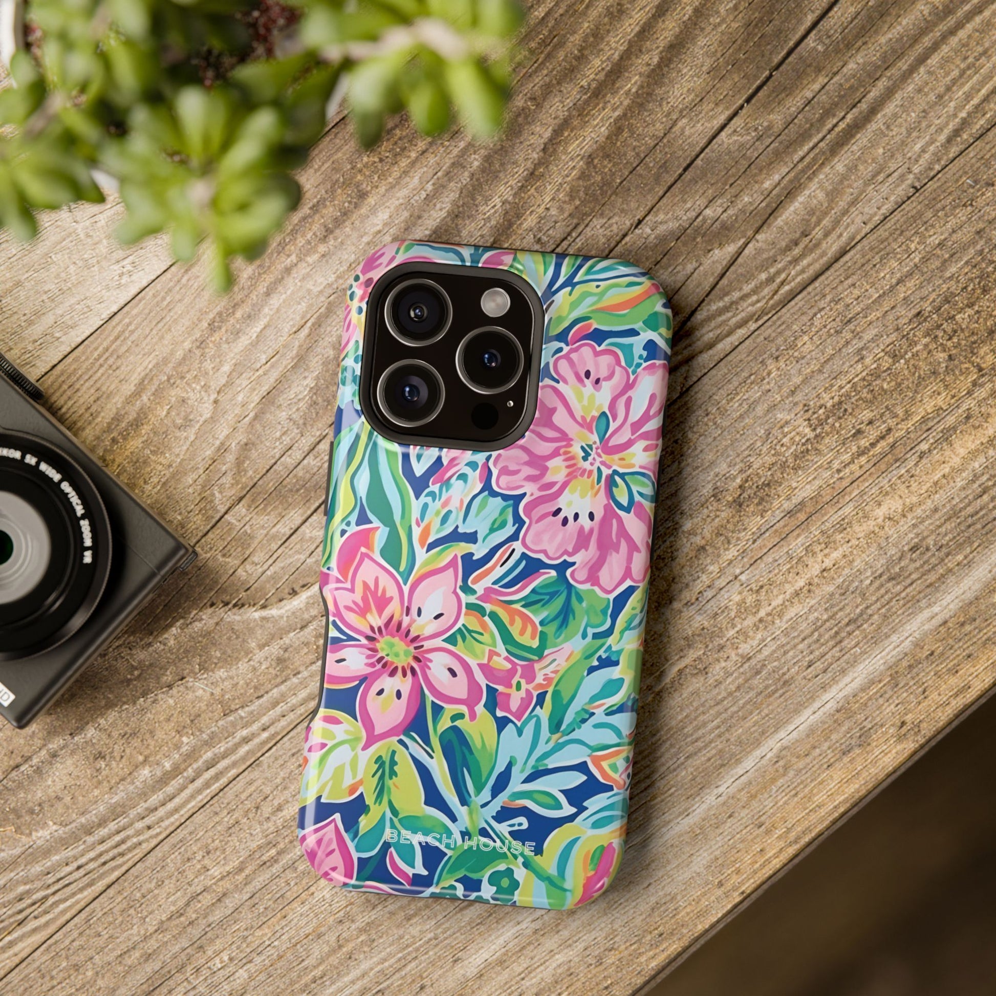 Floral Fernandina MagSafe Tough Case for iPhone on a wooden surface with a camera and plant in the background