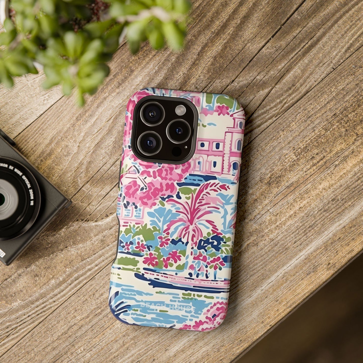 Amelia MagSafe Tough Case for iPhone on a wooden surface with a camera and plant in the background