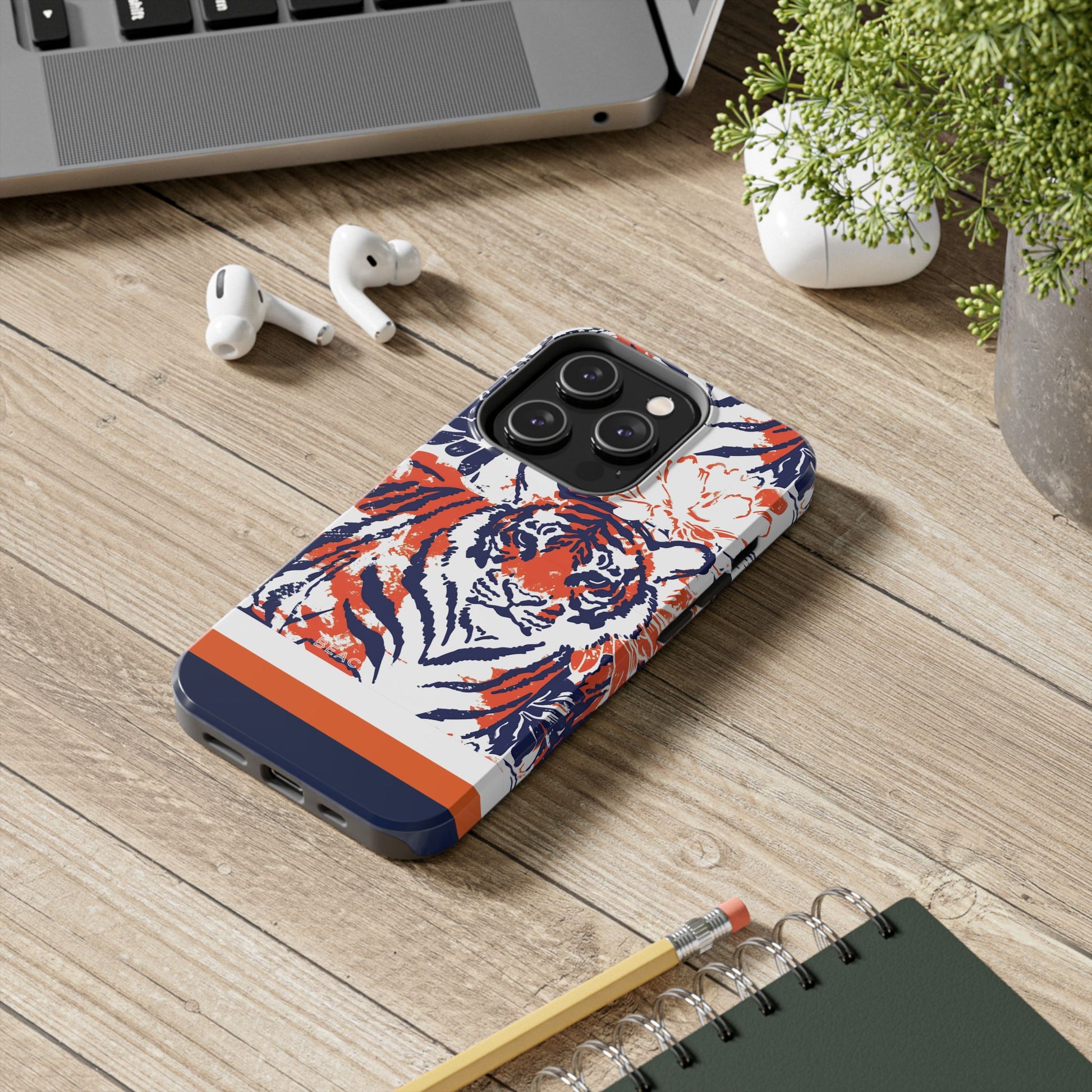 Auburn Tough Case for iPhone with tiger design on a wooden surface with laptop, earbuds, and notebook.