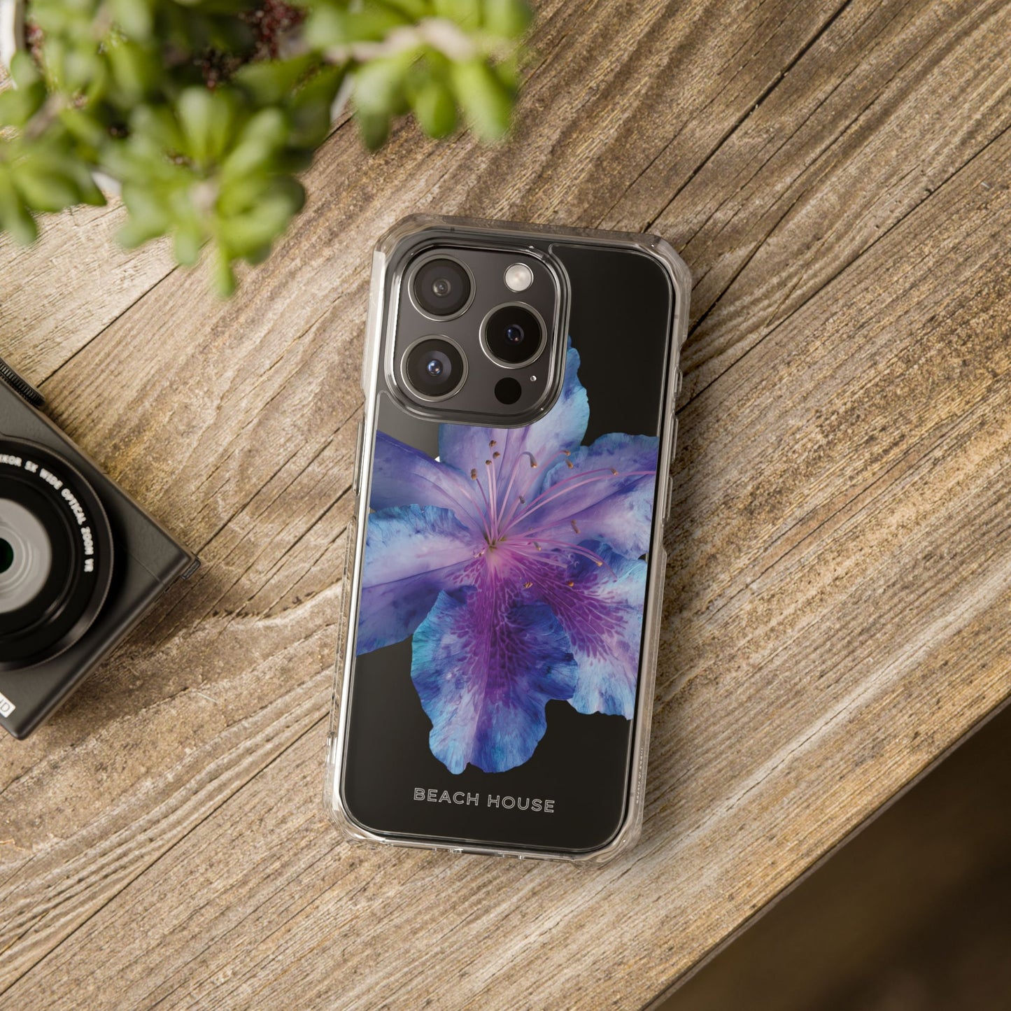 Phone case with floral design on a wooden surface next to a camera