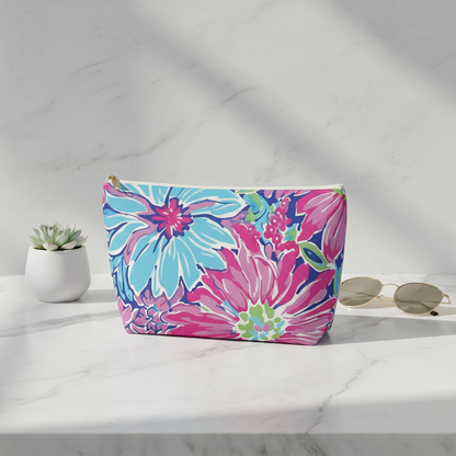 Floral patterned pouch on a white surface with sunglasses and a plant in the background