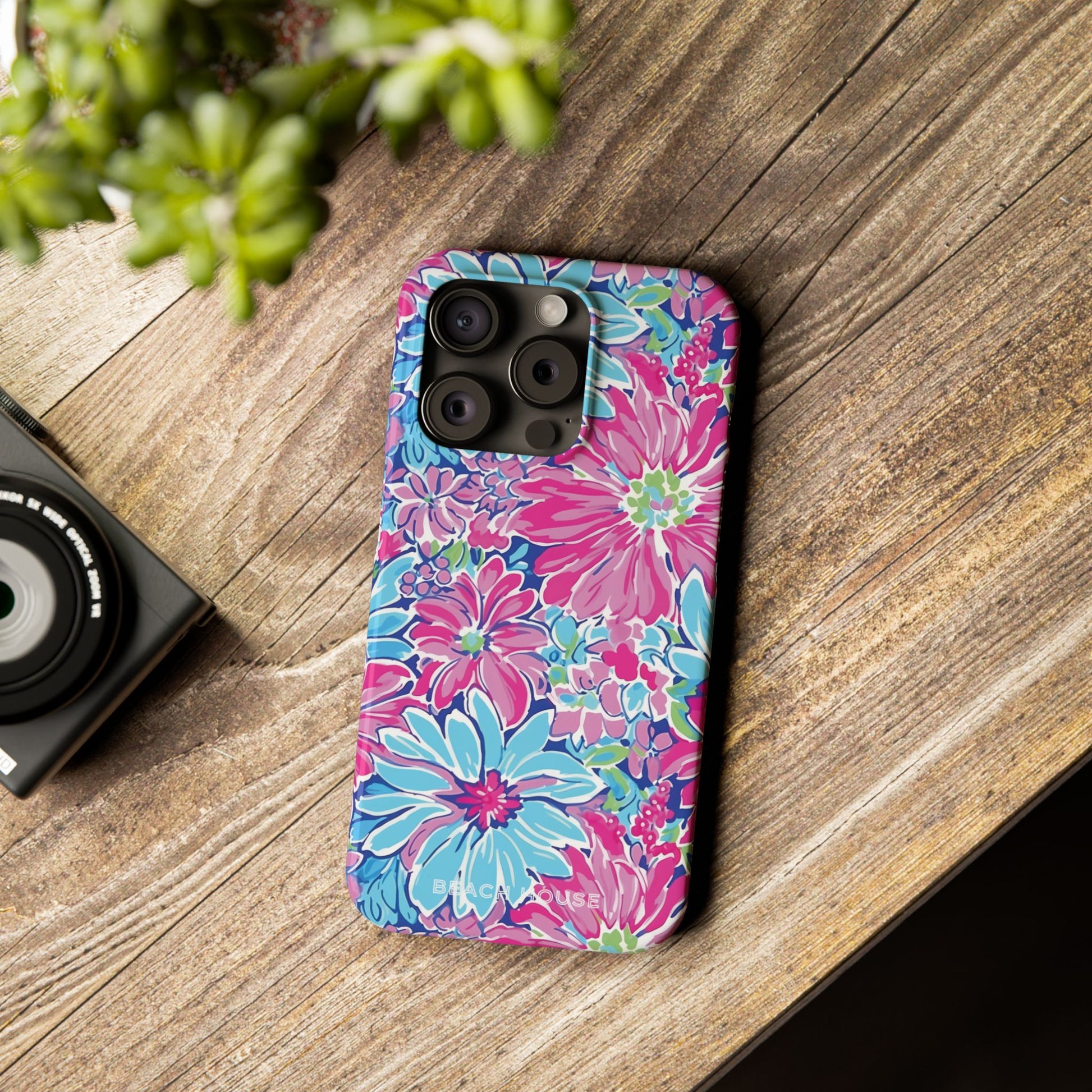 Bimini Slim Case for iPhone on a wooden surface with a camera and plant in the background