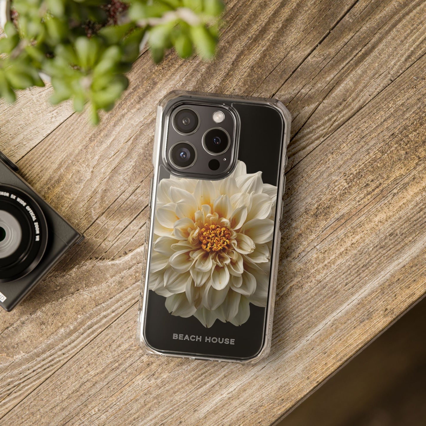 Phone case with a flower design on a wooden surface next to a camera