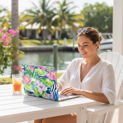 Woman using a laptop with a colorful floral Everglades MacBook Case outdoors by a waterfront.