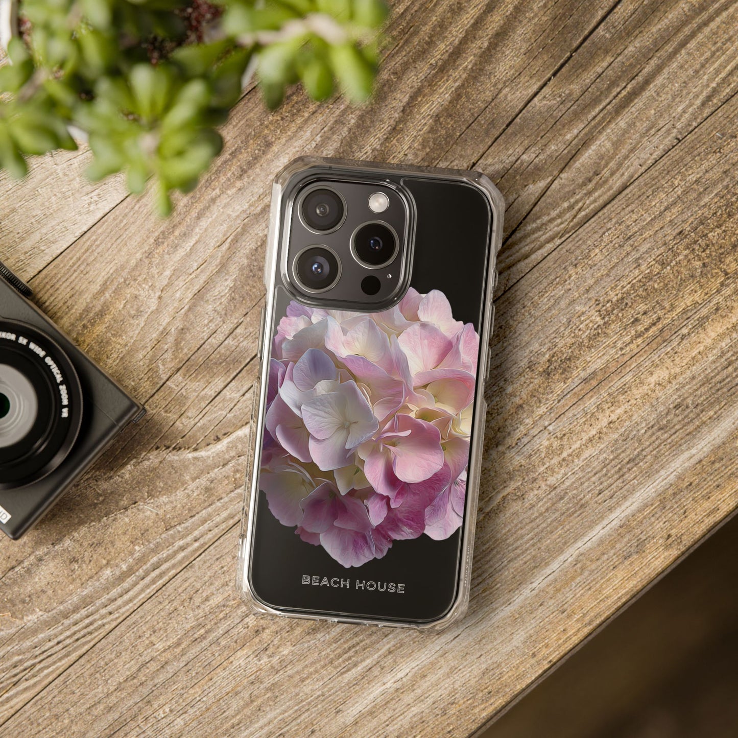 Phone case with floral design on a wooden surface next to a camera