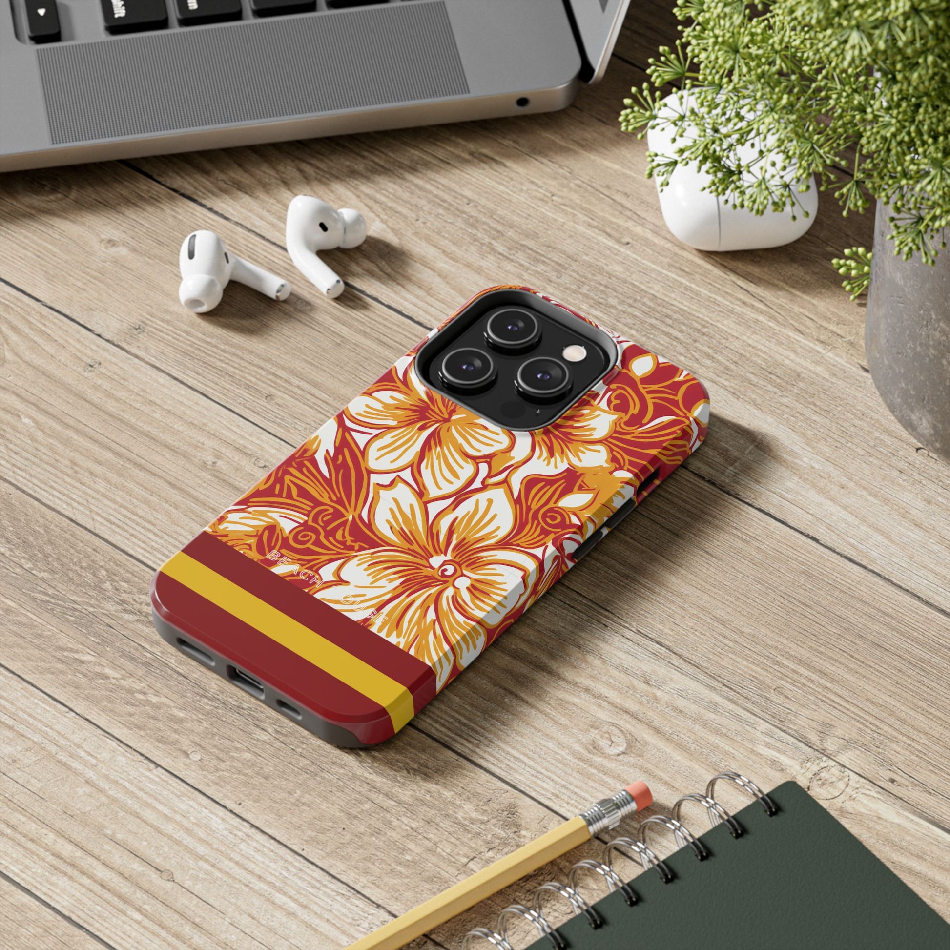 Los Angeles Tough Case for iPhone with floral design on a wooden desk with laptop, earbuds, and notebook.