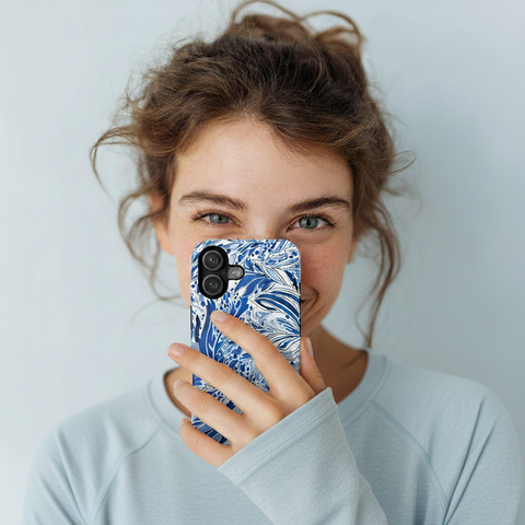 Woman holding a phone with a blue floral Nags Head phone case against a light background
