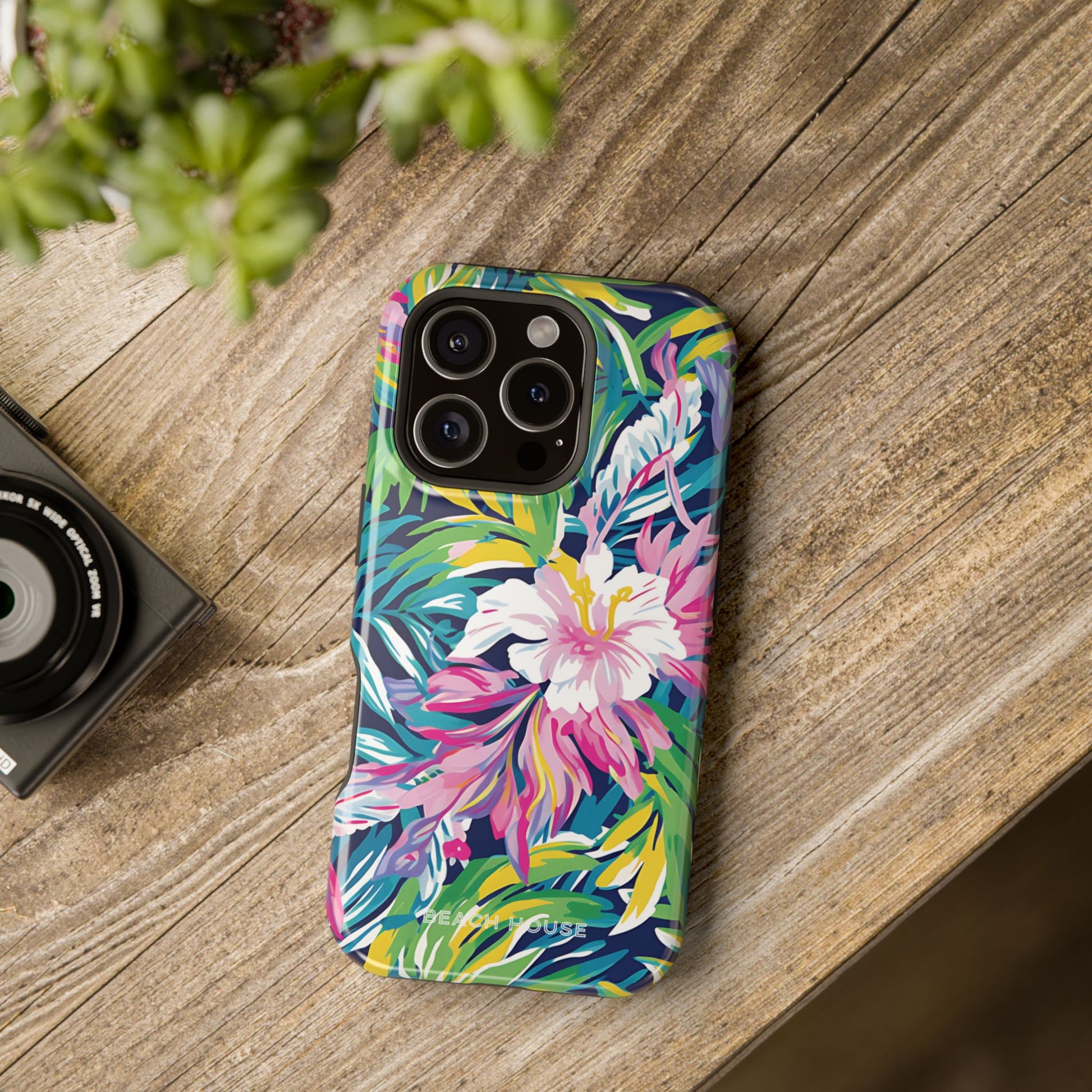 Colorful floral phone case on a wooden surface with a camera and plant in the background