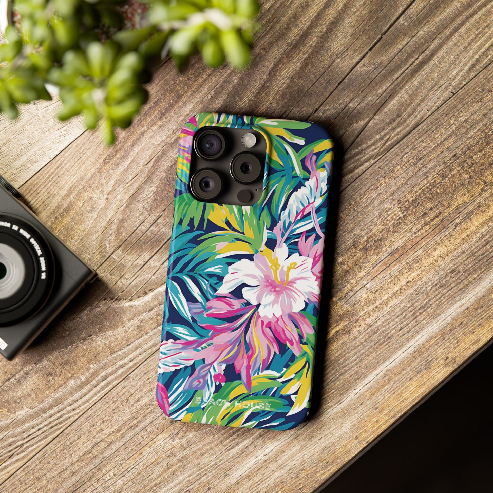 Phone case with colorful floral design on a wooden surface next to a camera