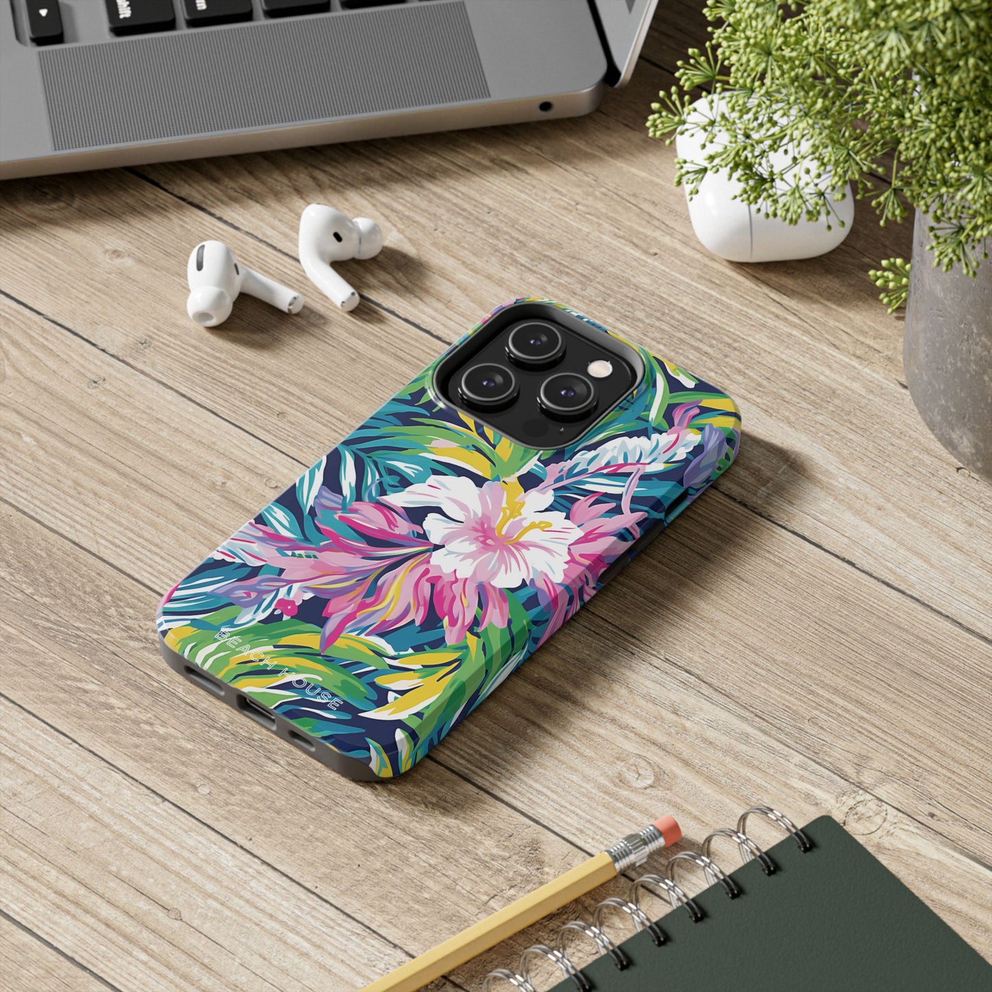Playa Hermosa Tough Case for iPhone with floral design on a wooden desk with laptop, earbuds, and notebook.
