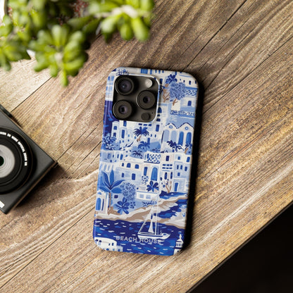 Santorini Slim Case for iPhone with blue and white design on a wooden surface next to a camera and plant.