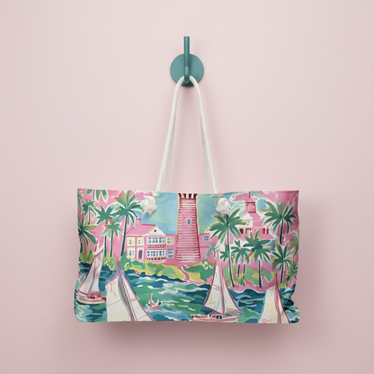 St. Simon Weekender Tote bag with a vibrant coastal scene design hanging on a hook against a pink background