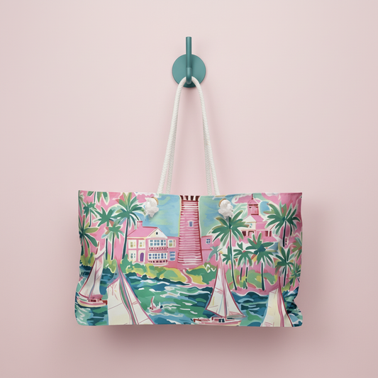 St. Simon Weekender Tote bag with a vibrant coastal scene design hanging on a hook against a pink background