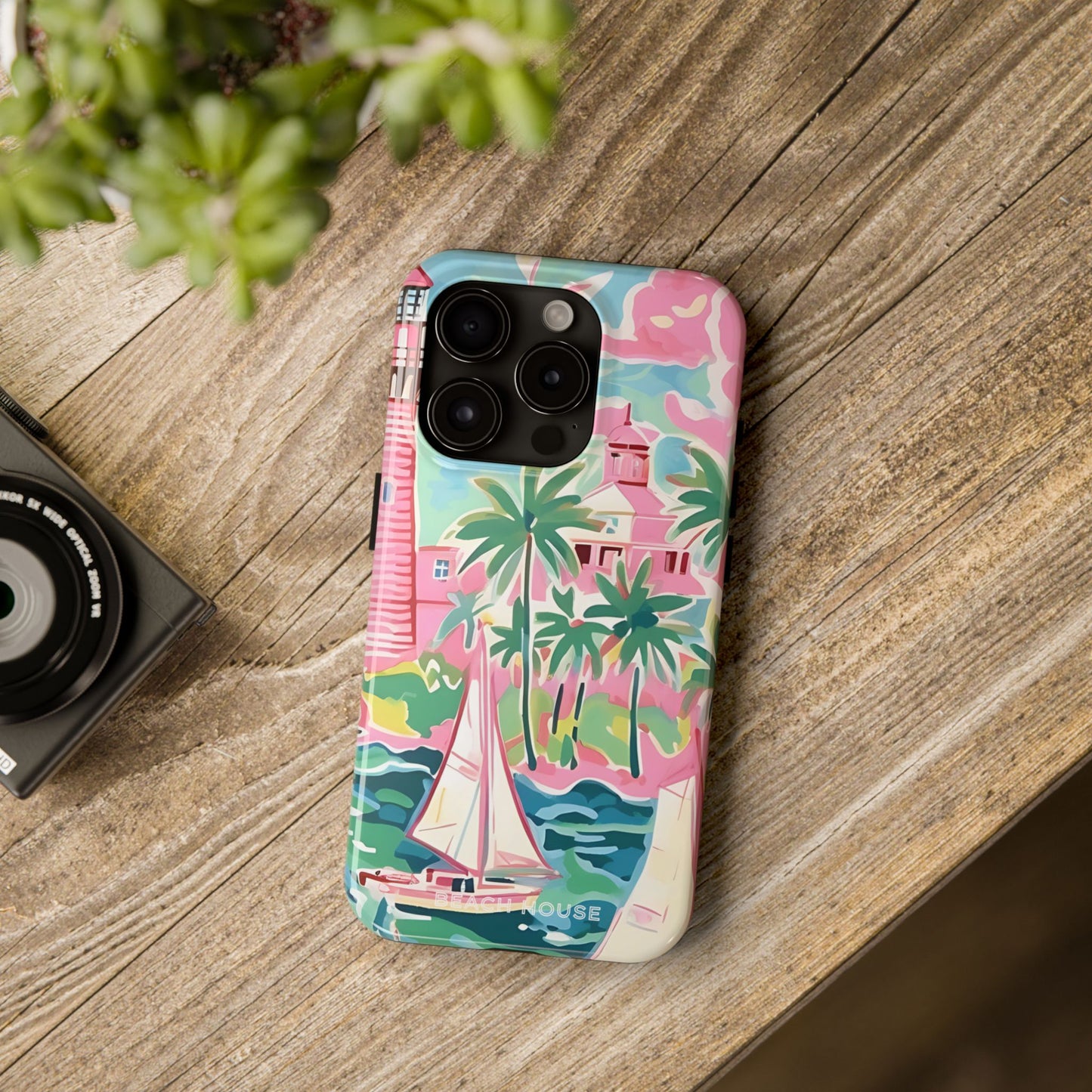St. Simon Phone case with pink, green, and blue coastal design on a wooden surface next to a camera