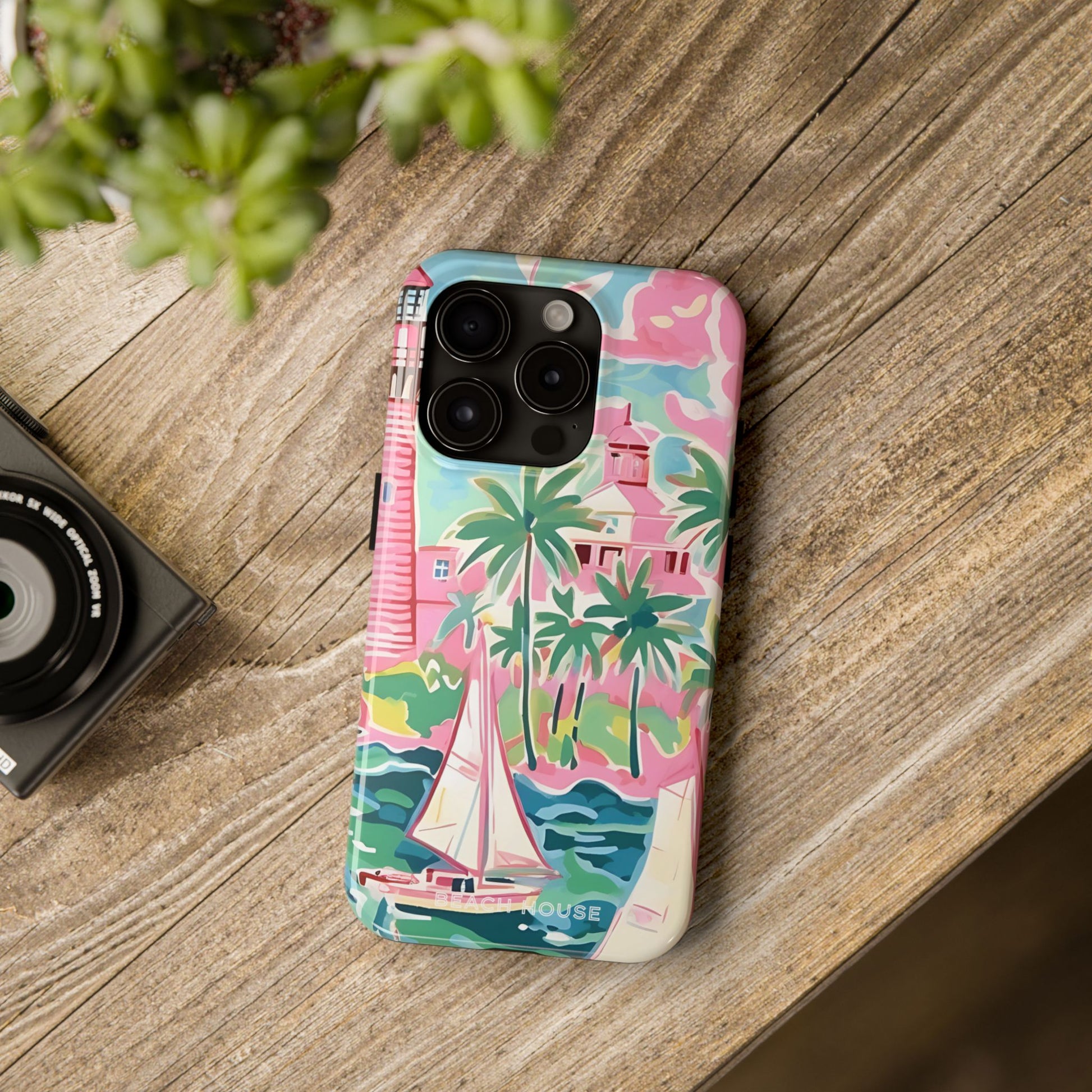 St. Simon Phone case with pink, green, and blue coastal design on a wooden surface next to a camera