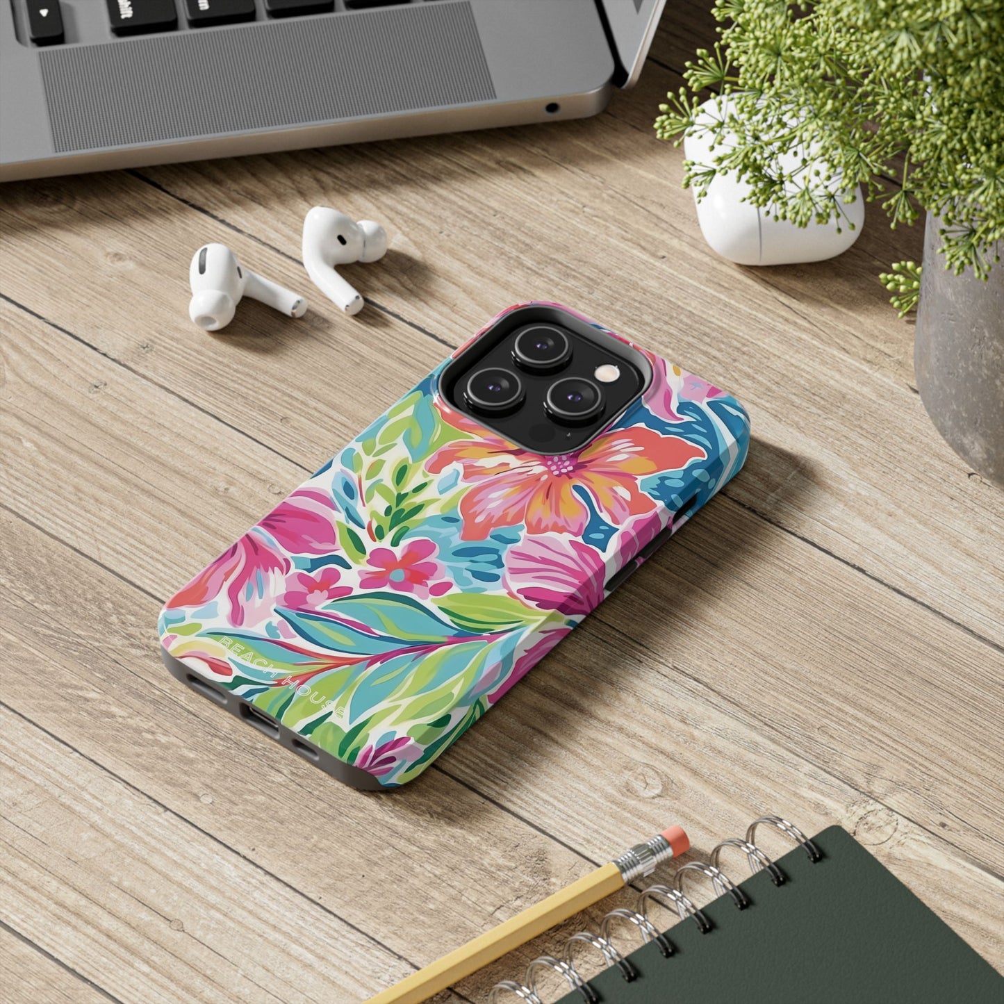 Colorful Waikiki phone case on a wooden desk with a laptop, earbuds, and notebook.